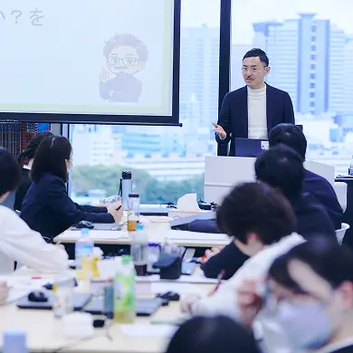 明るい会議室で対面に座る男女。女性は黒い書類フォルダを手に男性に向かって微笑み、男性は後ろ姿寄りで女性を見ている。窓の外にビル街、白い壁にはモニターが掛かっている