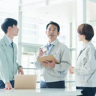 作業服を着た男女3名が仕事の打ち合わせをしている